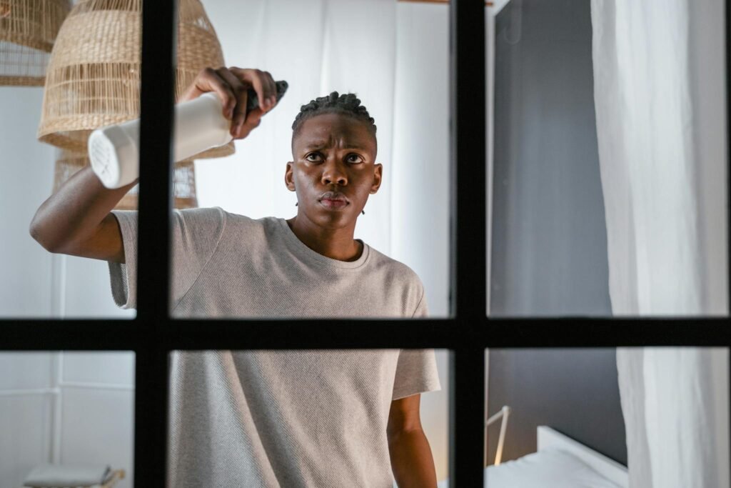 A young man cleaning a window indoors with a spray bottle, focusing on household chores.